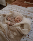 Baby wrapped in a blanket on a bed with a wooden nightstand in the background