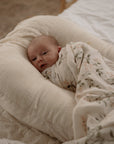 Newborn baby wrapped in a floral blanket swaddle laying on a newborn bassinet.