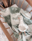 Baby blanket with leaf pattern and plush duck toy on a wooden surface