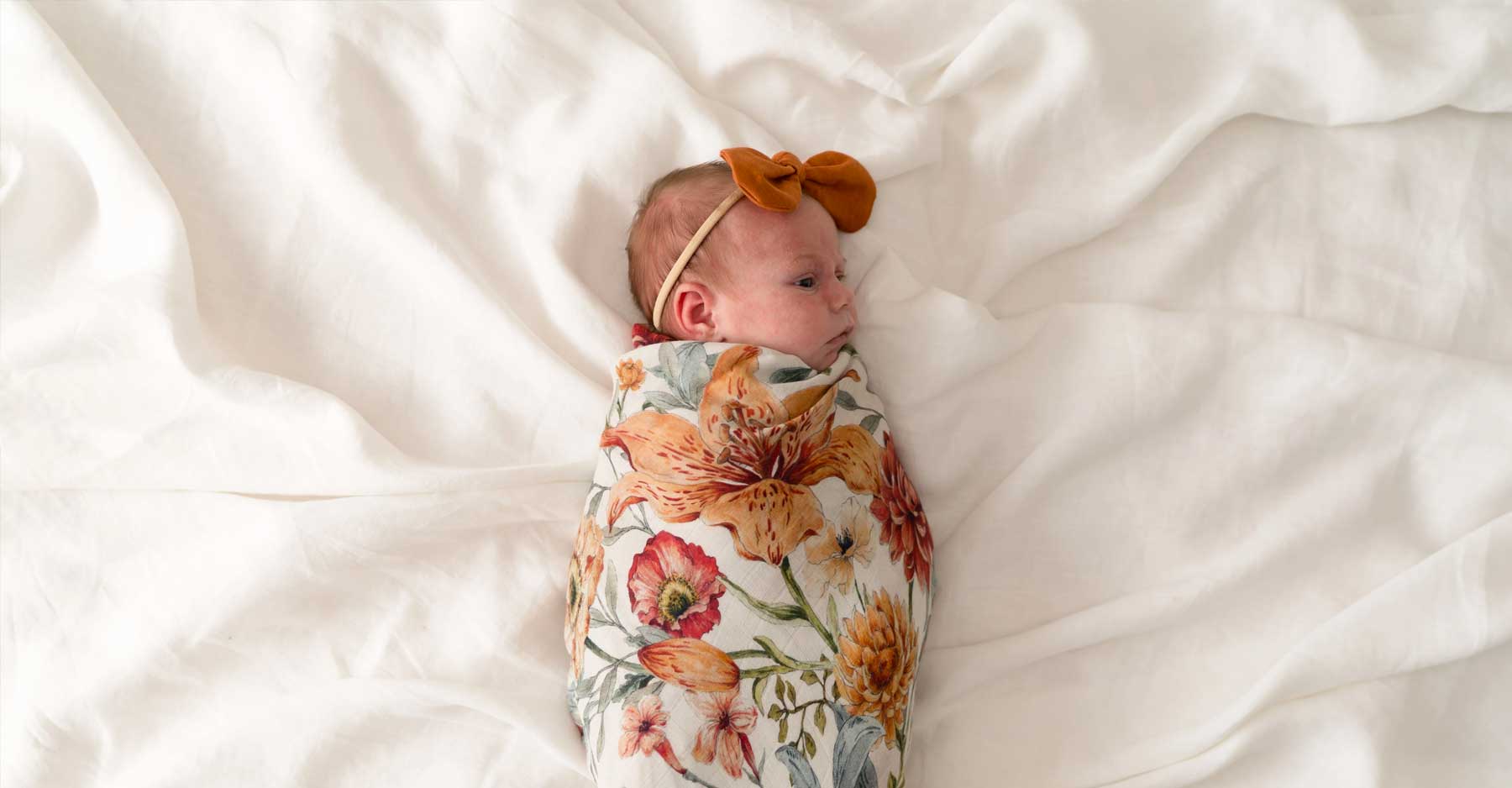 Newborn baby boy swaddled in fabric sleeping and holding his hands close to cheeks.