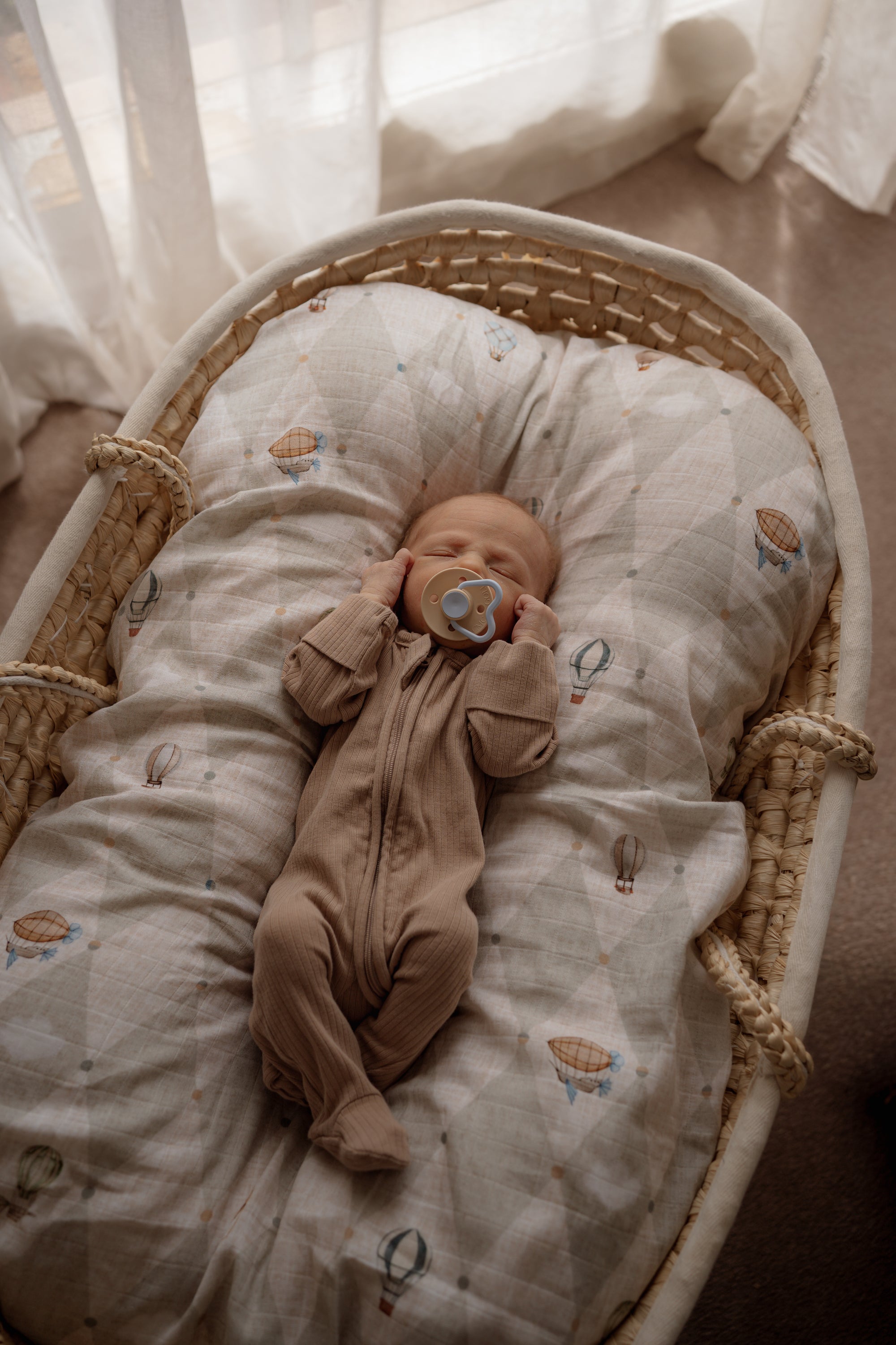 Sleeping baby in a moses basket with a swaddle and dummy.