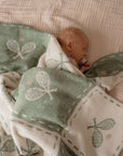 Baby wrapped in a green blanket with tennis patterns on a checkered bed.