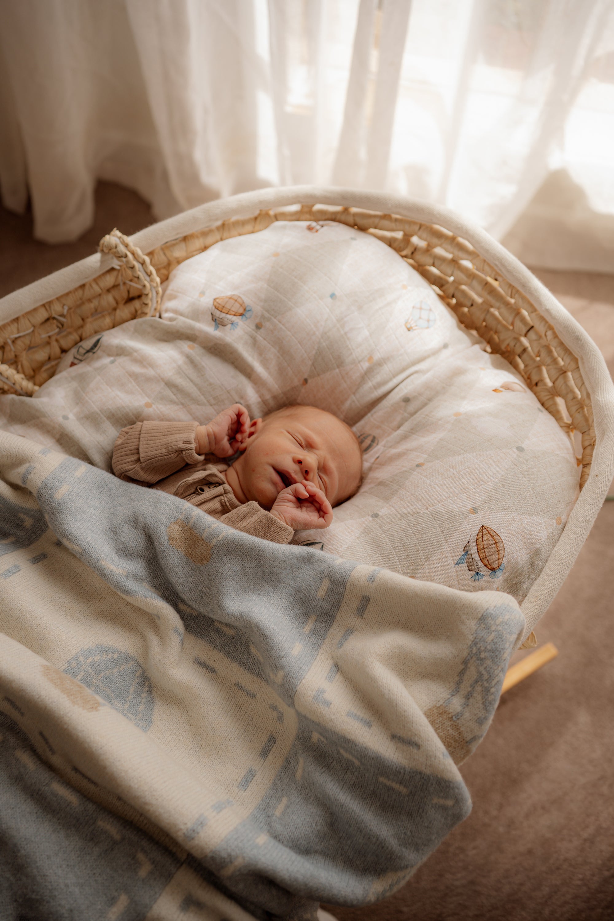Newborn baby sleeping in a bassinet with a soft blanket and pillow.