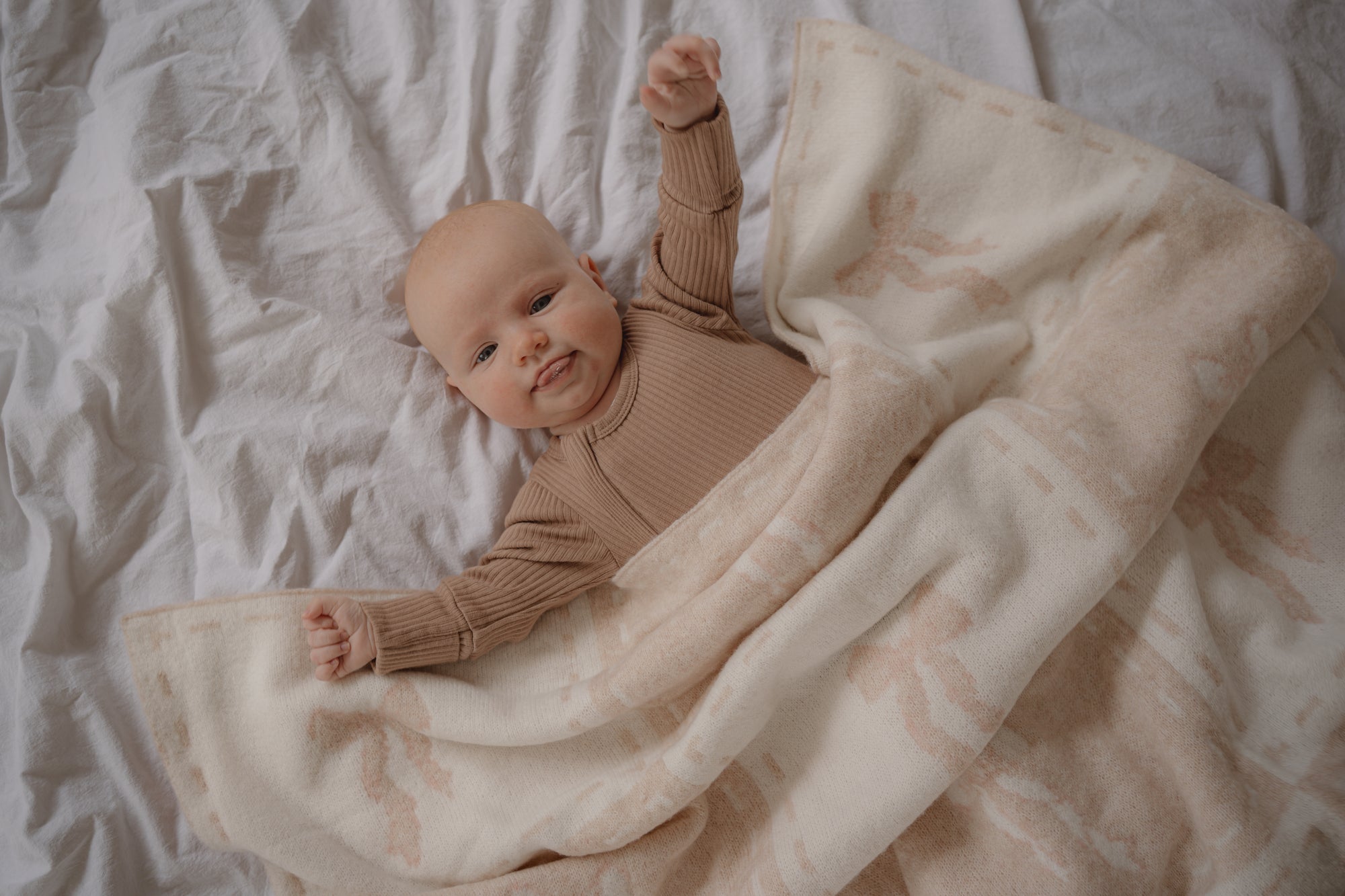 Baby in a brown outfit lying on a white blanket