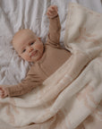 Baby in a brown outfit lying on a white blanket