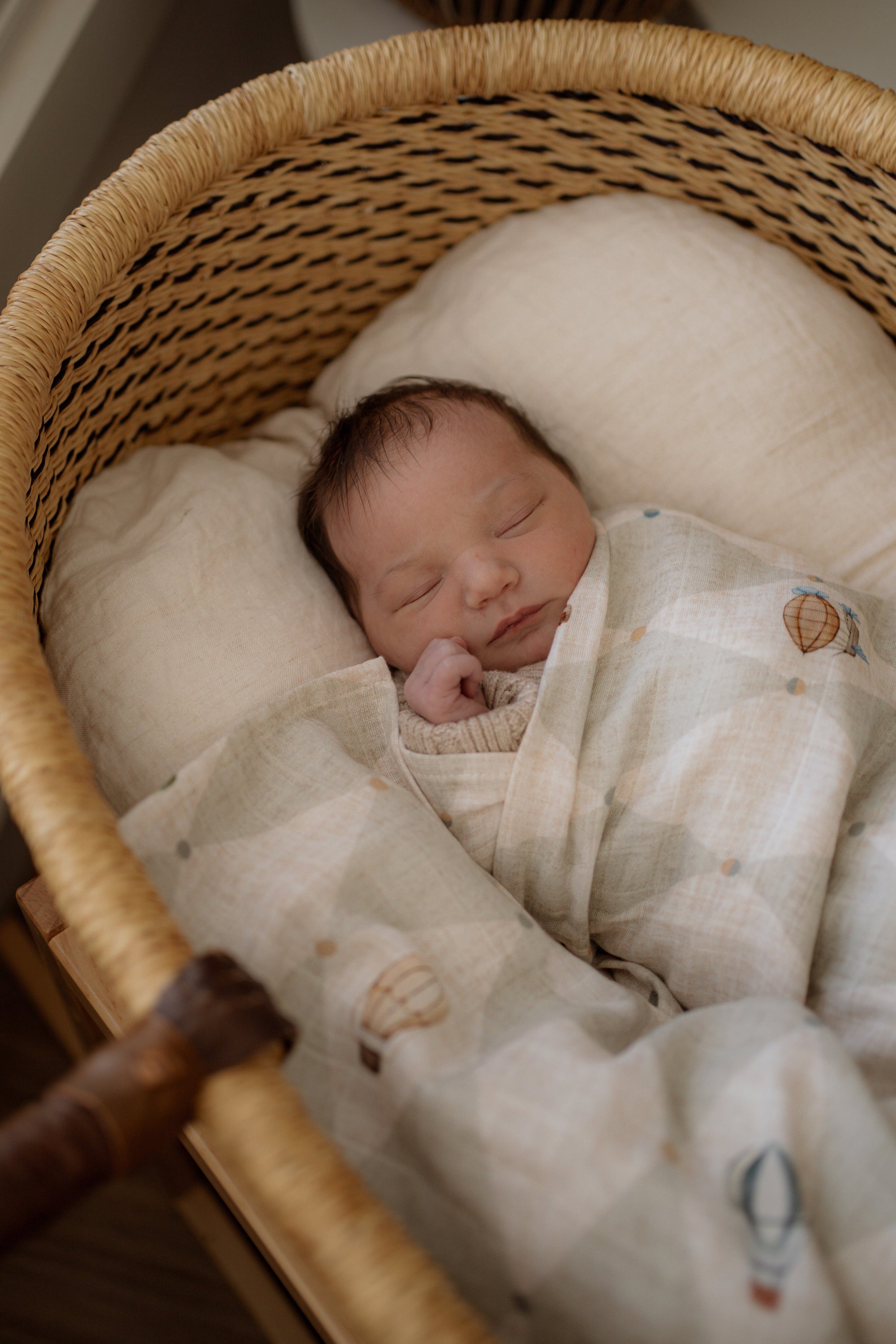 Newborn baby sleeping in a wicker bassinet with a soft blanket.