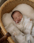 Newborn baby sleeping in a wicker bassinet with a soft blanket.