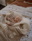 Baby wrapped in a blanket on a bed with a wooden nightstand in the background