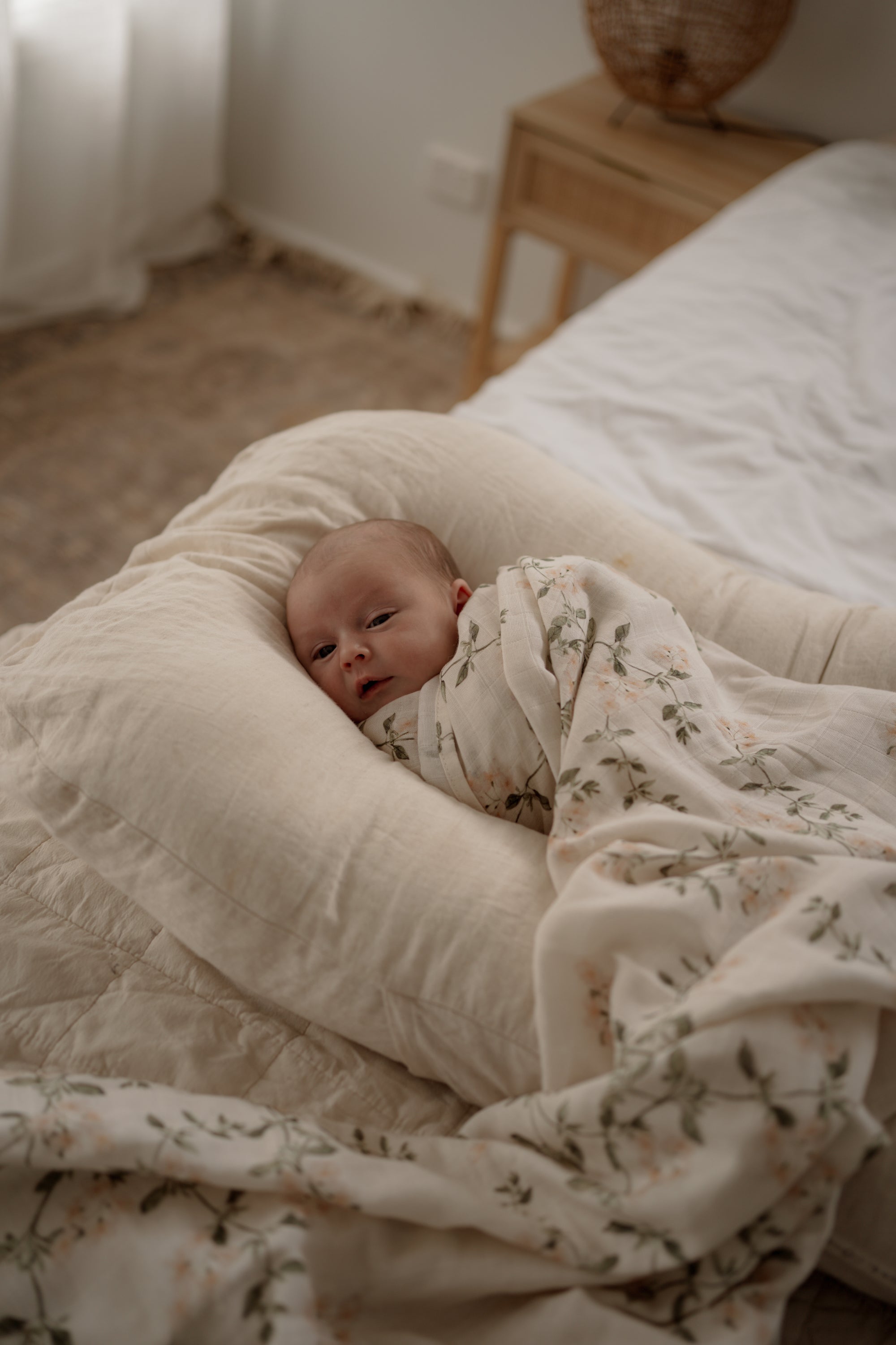 Newborn baby wrapped in a floral blanket lying on a soft pillow in a cozy room.