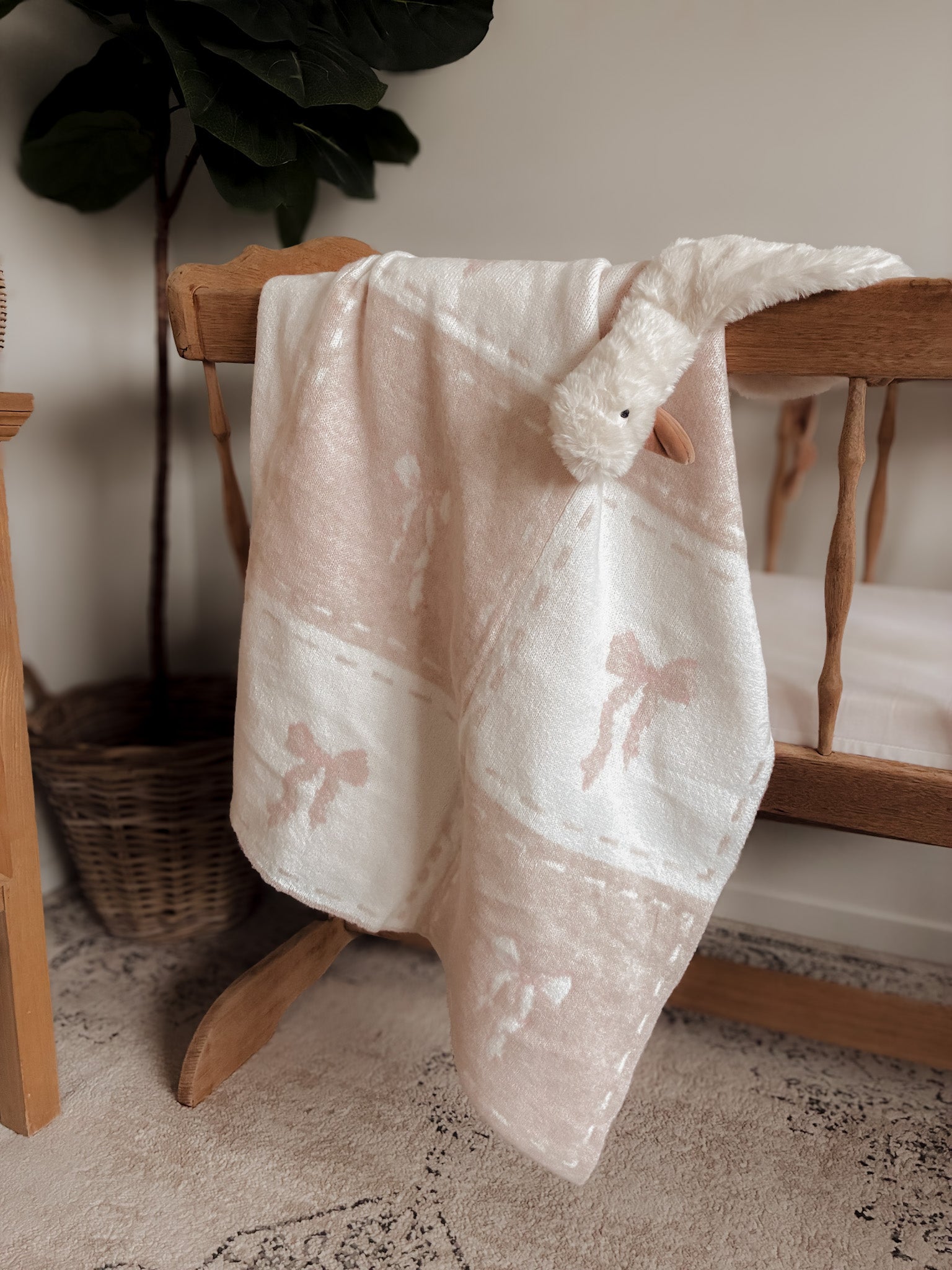 White bow baby blanket draped over a wooden cradle with a plant in the background