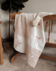 White bow baby blanket draped over a wooden cradle with a plant in the background