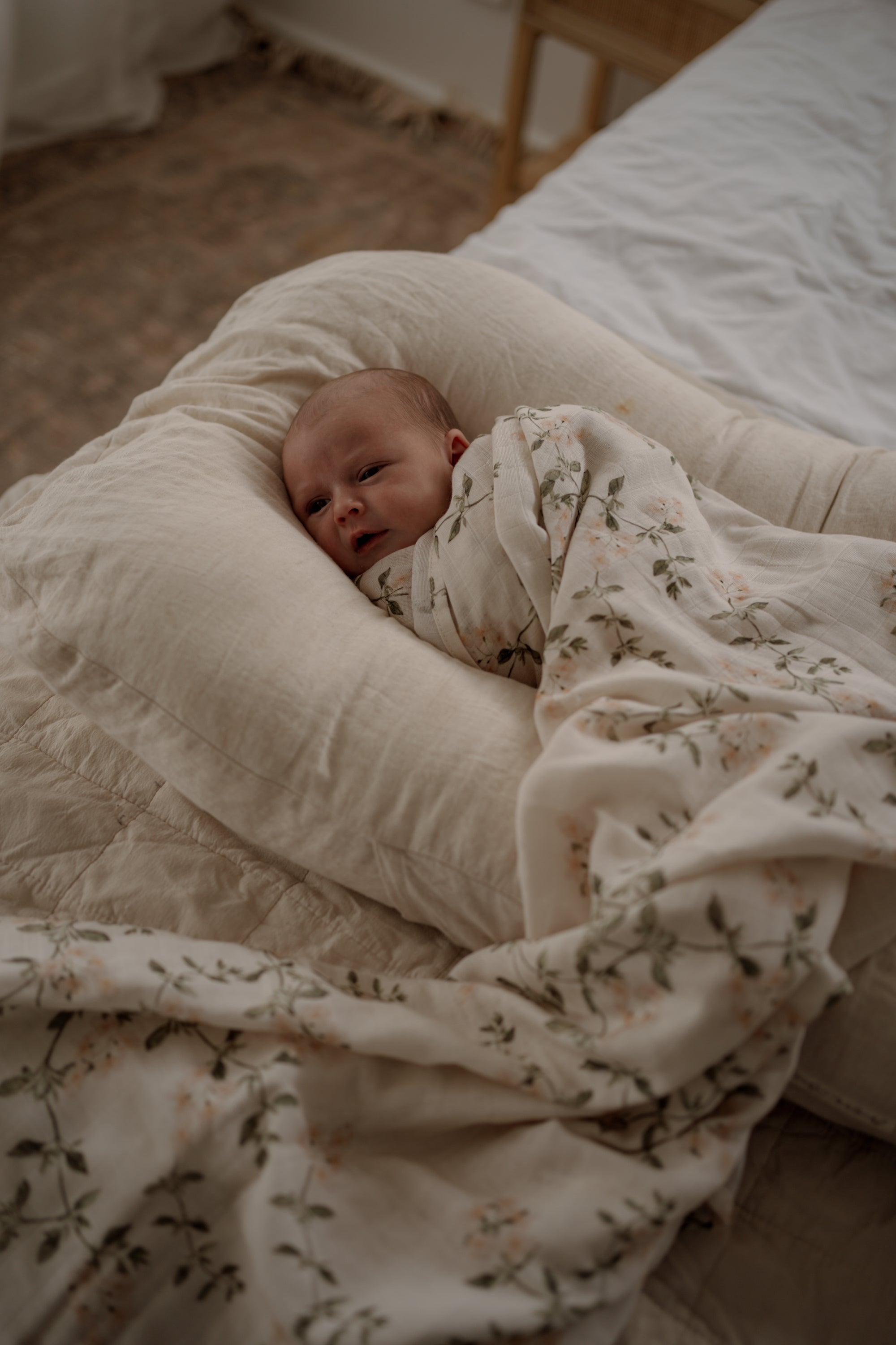 Newborn baby wrapped in a floral blanket lying on a soft pillow in a bedroom.
