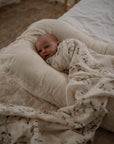 Newborn baby wrapped in a floral blanket lying on a soft pillow in a bedroom.
