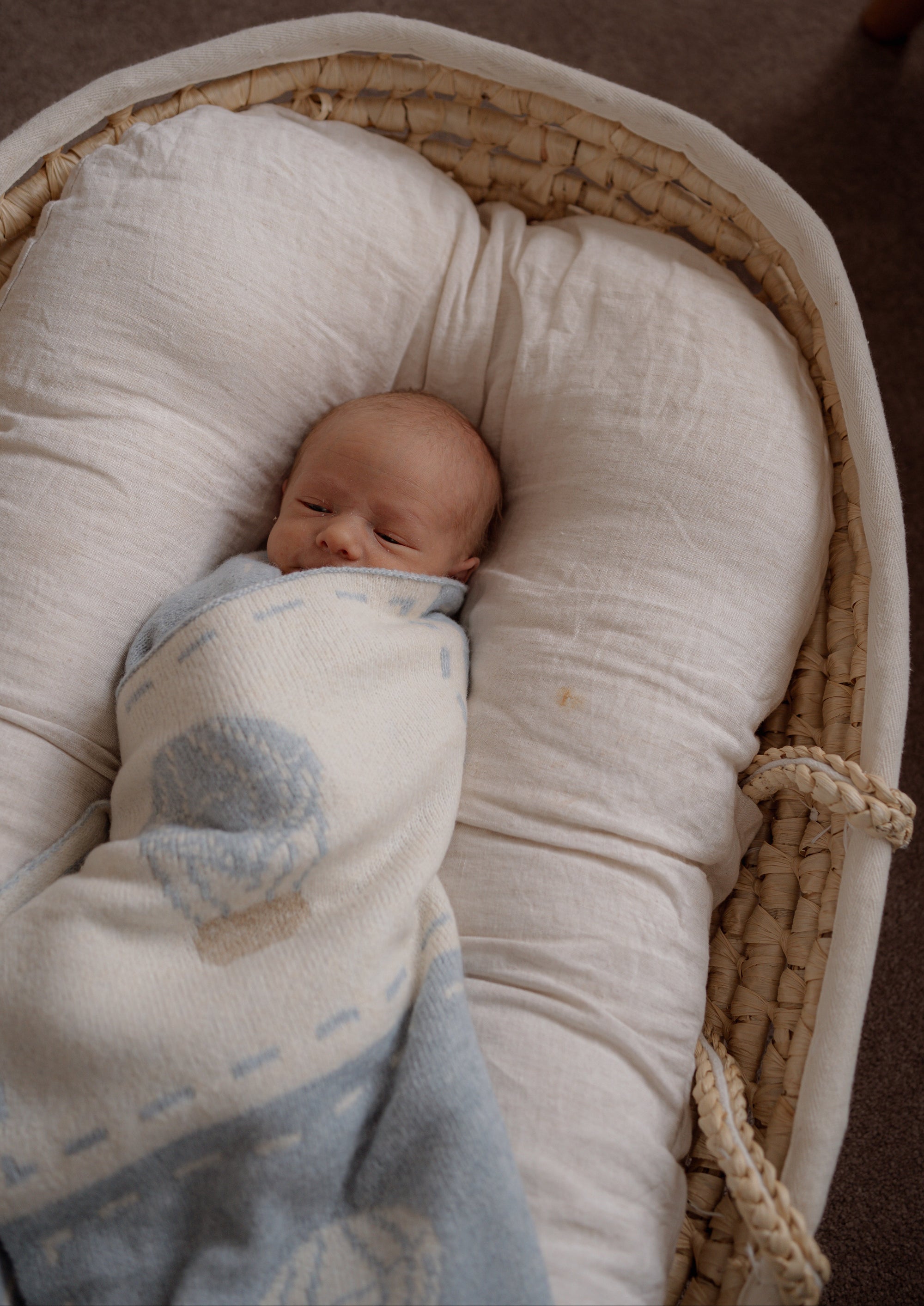 Newborn baby wrapped in a hot air balloon blanket lying in a woven basket.