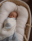 Newborn baby wrapped in a hot air balloon blanket lying in a woven basket.