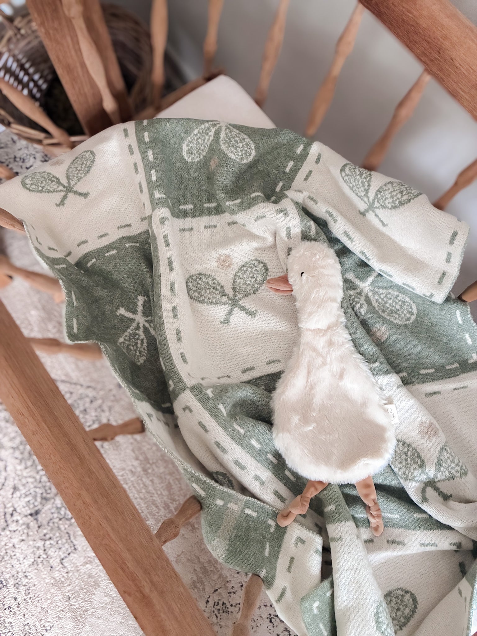Baby blanket with leaf pattern and plush duck toy on a wooden surface