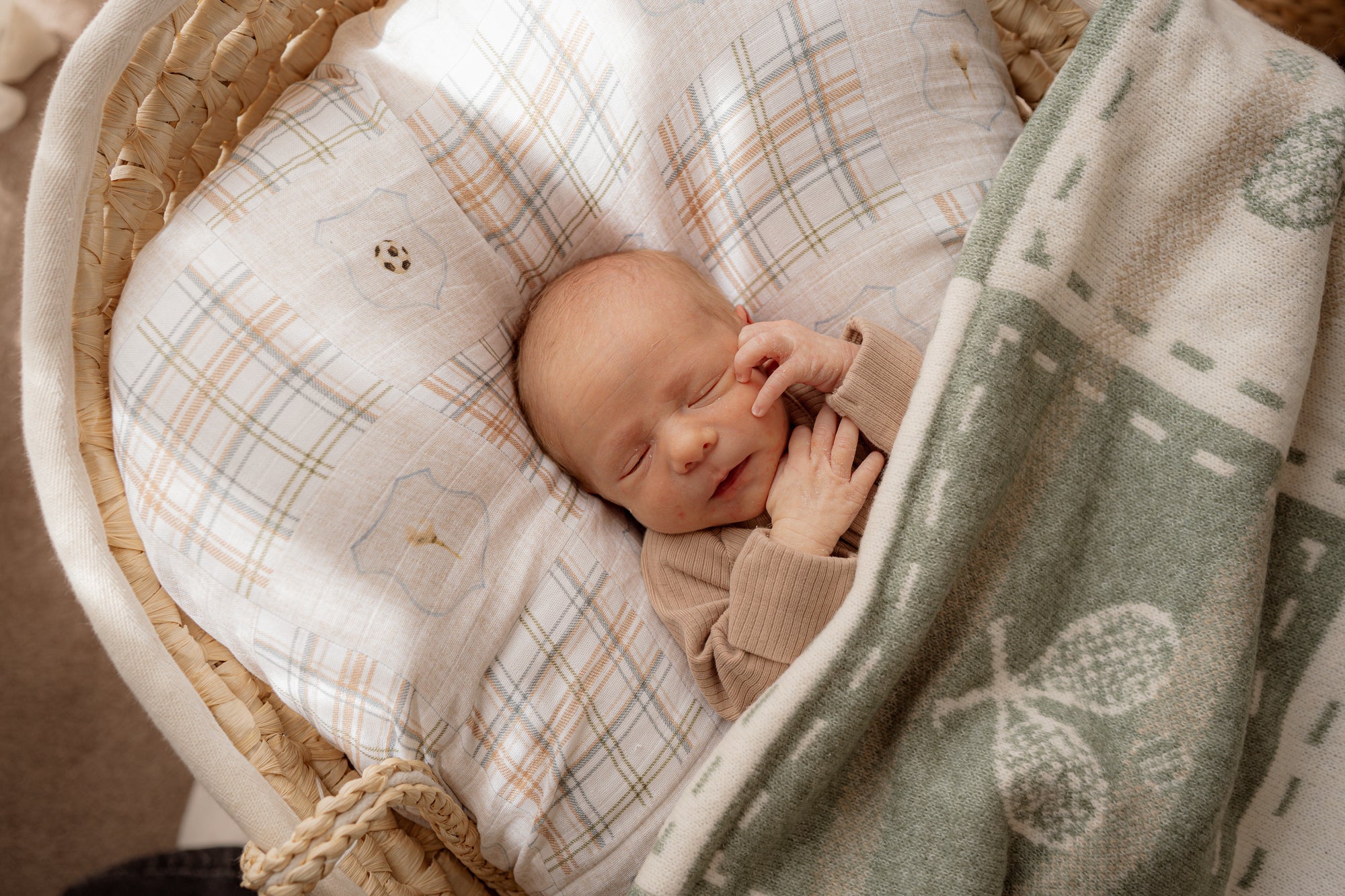 Newborn baby sleeping in a basket with plaid and green blankets